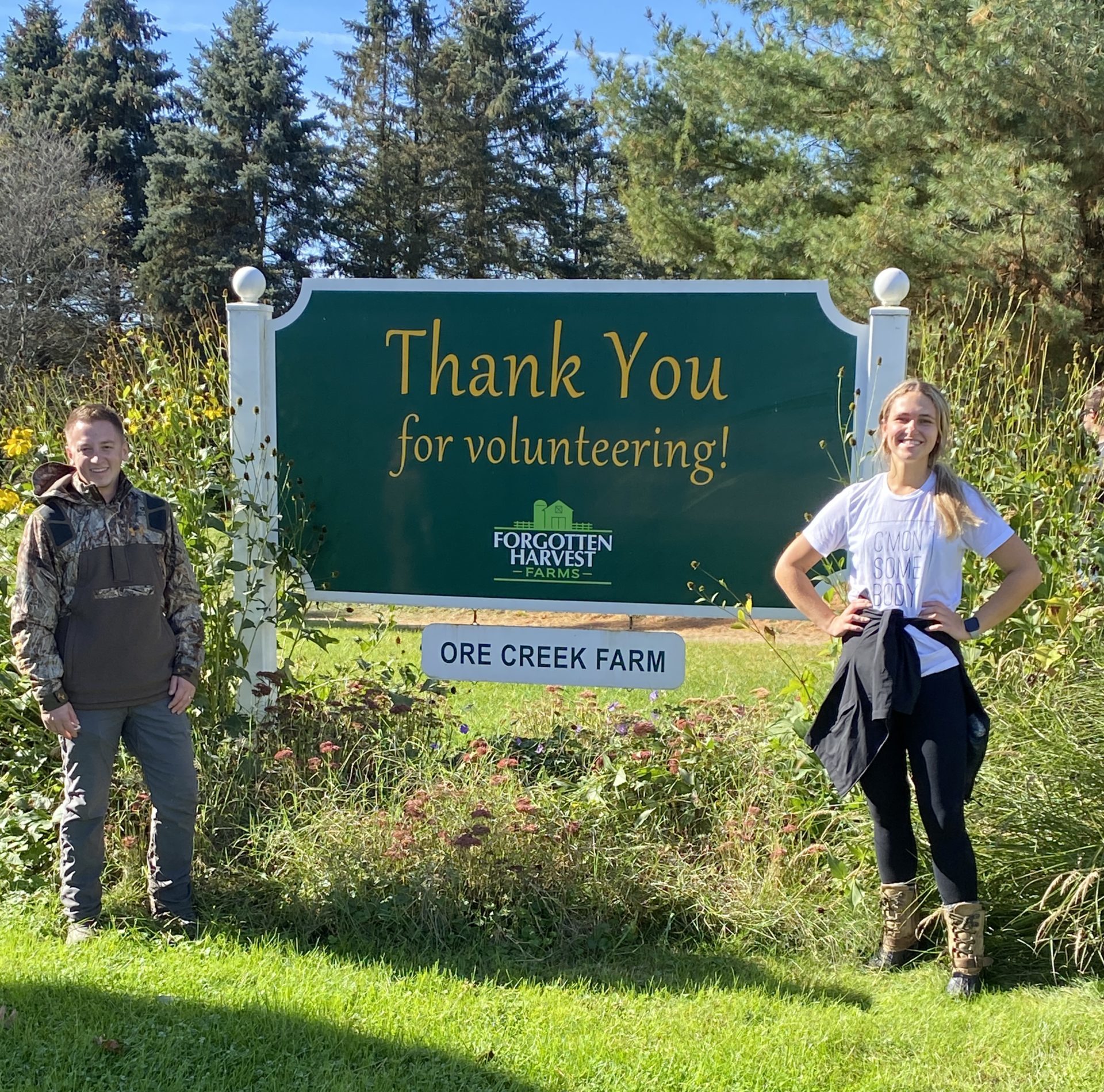 SGCI members stand on opposite sides of a sign that reads, Thank You for Volunteering - Forgotten Harvest Farms - Ore Creek Farm.